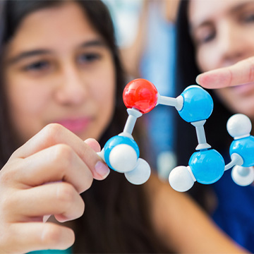 Two female middle schoolers holding up atoms figure