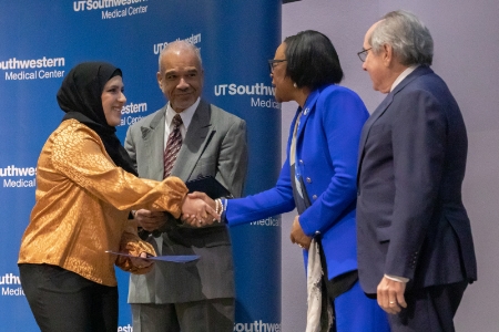 Two women shaking hands and smiling while standing next to two men with UTSW blue backdrop