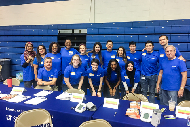 Student volunteers from the School of Health Professions line up behind a table at a community event