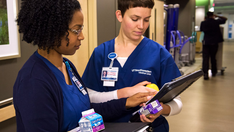 Nutrition students holding milk carton and an apple look at a patient's chart