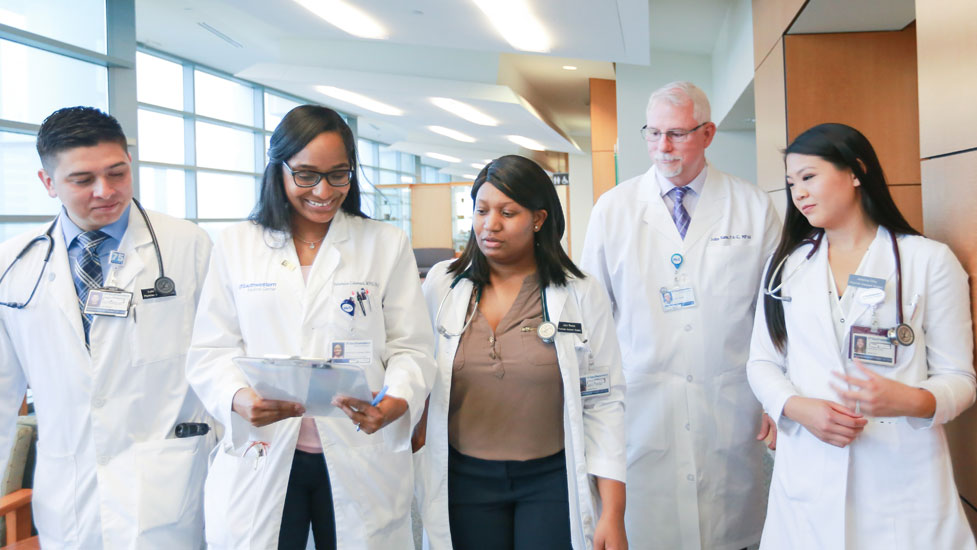 Students in lab coats with faculty walking in the hallway