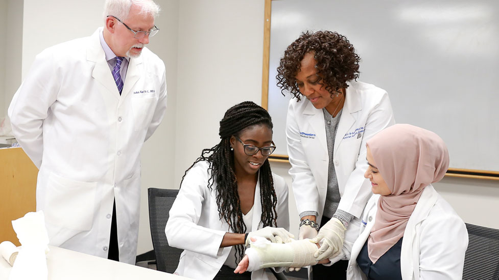 Student wrapping another student's arm with professor overseeing