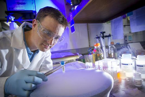 Lab setting with male technician who is holding a vial with long tweezers