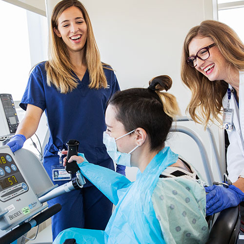 Two female students watch as another student works with physical therapy equipment