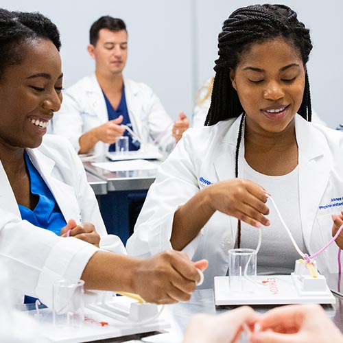 Two female and a male physician assistant studies students learn to suture