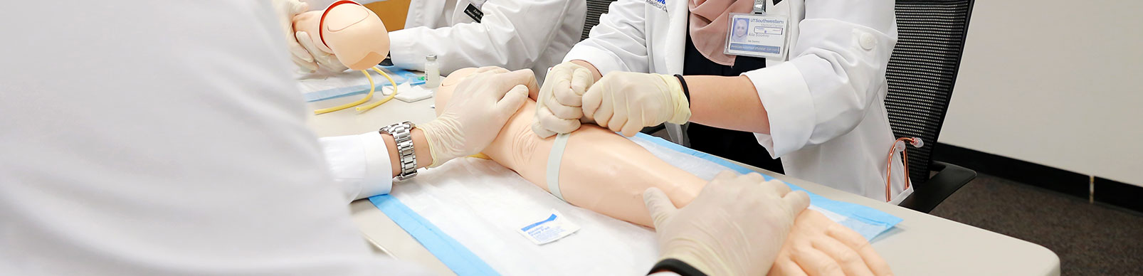 Students wearing gloves learn to use a tourniquet on a model of a forearm