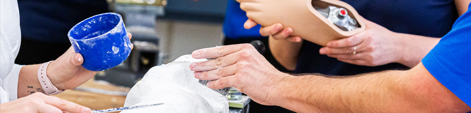 One person holds a blue jar, another person applies plaster to a mold while another person holds a prosthetic foot