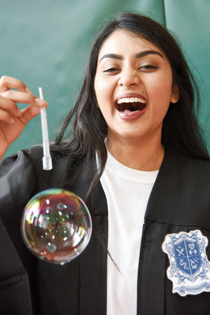 A woman laughs as a bubble floats from the pipette she holds
