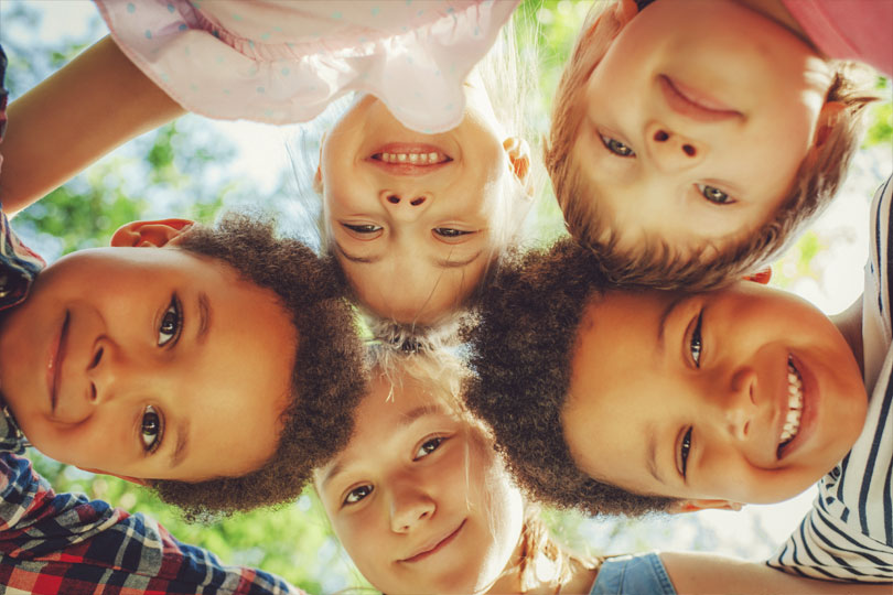 Five young children put their heads together to form a circle while looking down at the camera