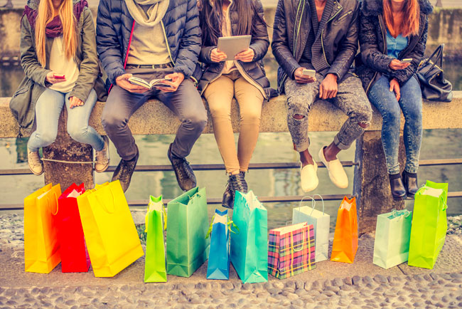 Group of young adults sitting on a bench with shopping bags at their feet