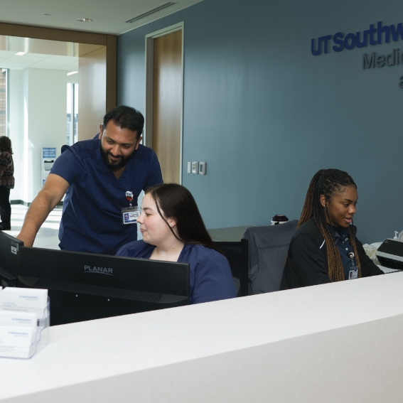 Three employees working at computers behind a counter.