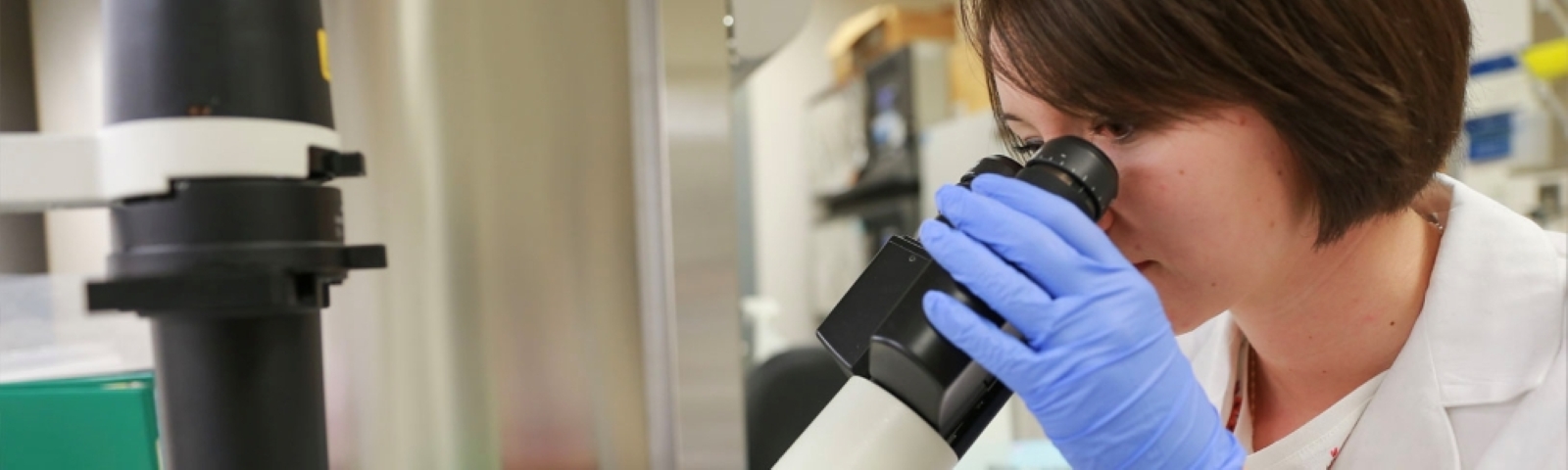 female student with short hair in lab looks thru microscope
