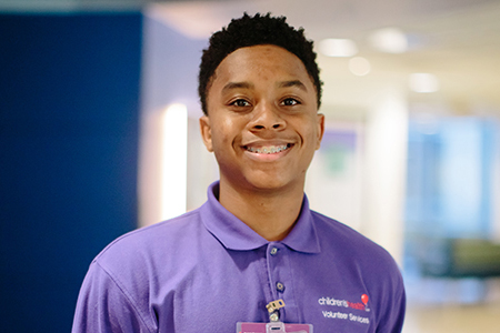 A young Black man smiling and wearing a purple Children's Health Volunteer shirt