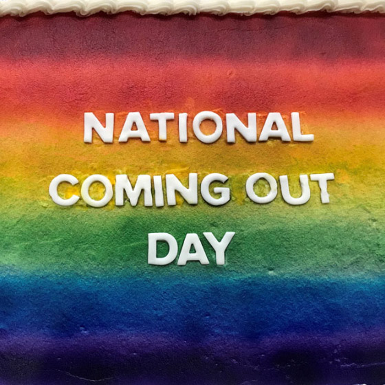A rainbow striped cake with National Coming Out Day written on it