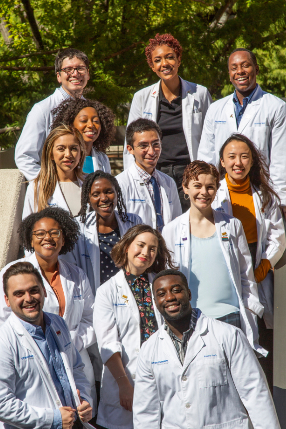 13 medical students standing on stairs and wearing their white coats
