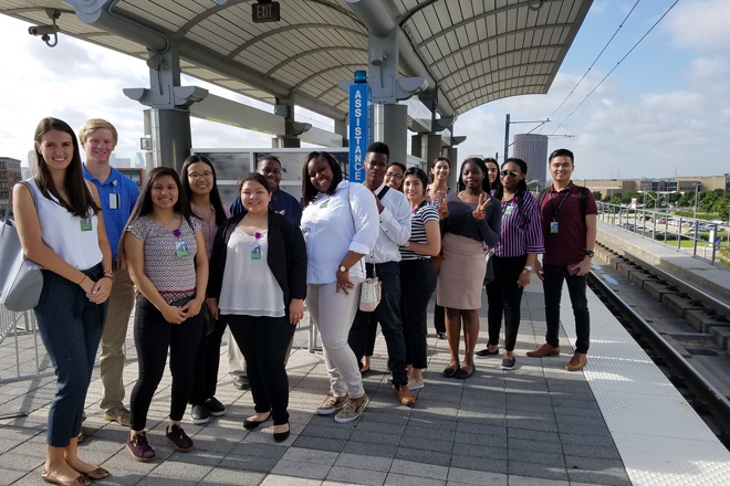 15 students stand at a train station in Dallas