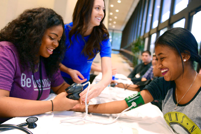 A female high school student learns to take blood pressure on another female student.