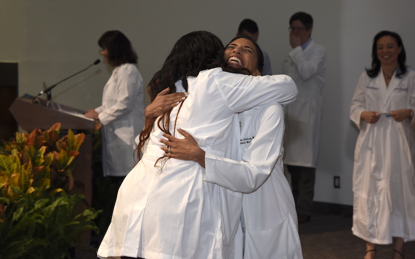 A female student hugs a female advisor when she gets her white coat