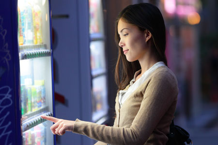 A young dark-haired woman pushes a button to select an item from a vending machine