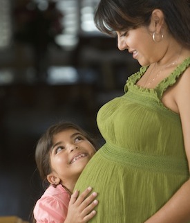 A pregnant woman smiles at her young daughter