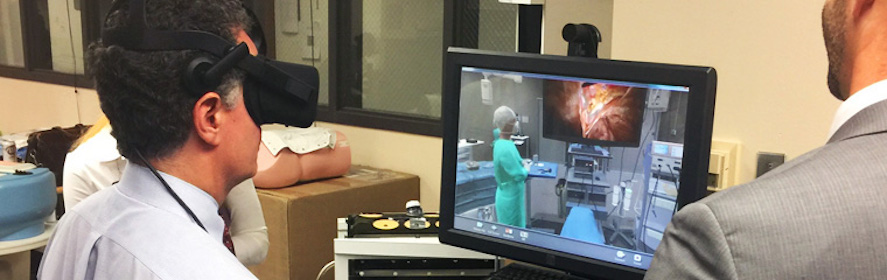 Dr. Daniel Scott, Simulations Center Director, engages in a hands-on demonstration of a virtual reality simulator that uses a head-mounted display to allow surgeons to practice operations in an immersive environment.