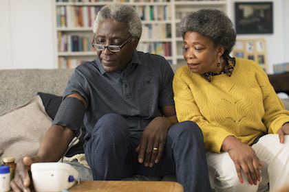 Woman watches a man check his blood pressure at home