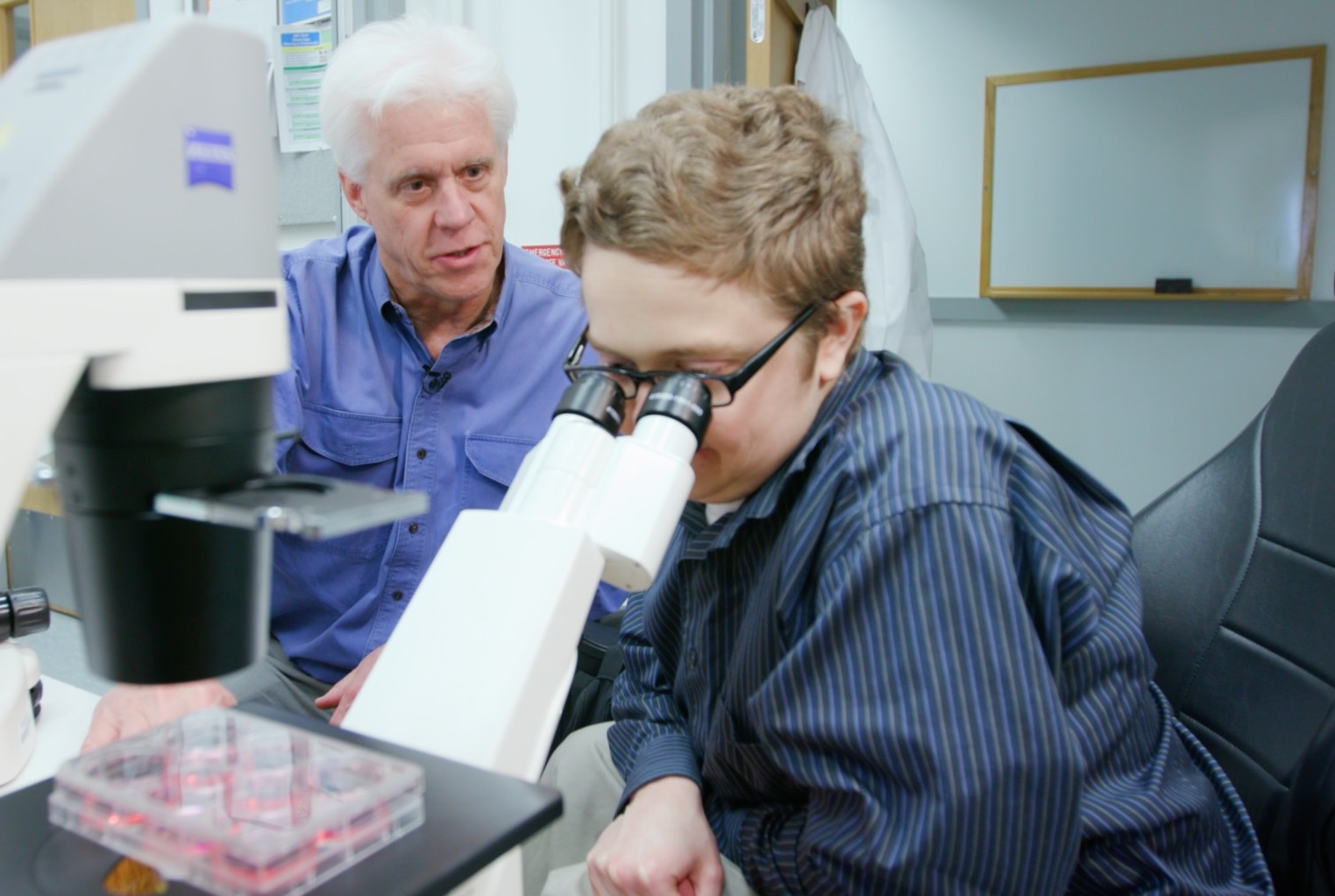 Ben Dupree looks through a microscope during a visit to the lab of Dr. Eric Olson, left