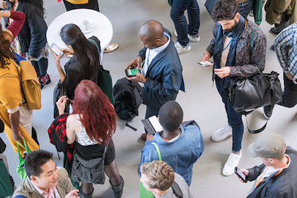 A diverse group of peope looking down at their phones and devices