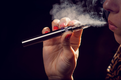 A young woman holds a vaping device near her mouth and exhales vapors