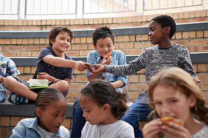 School-age boys and girls sit on risers and share snacks