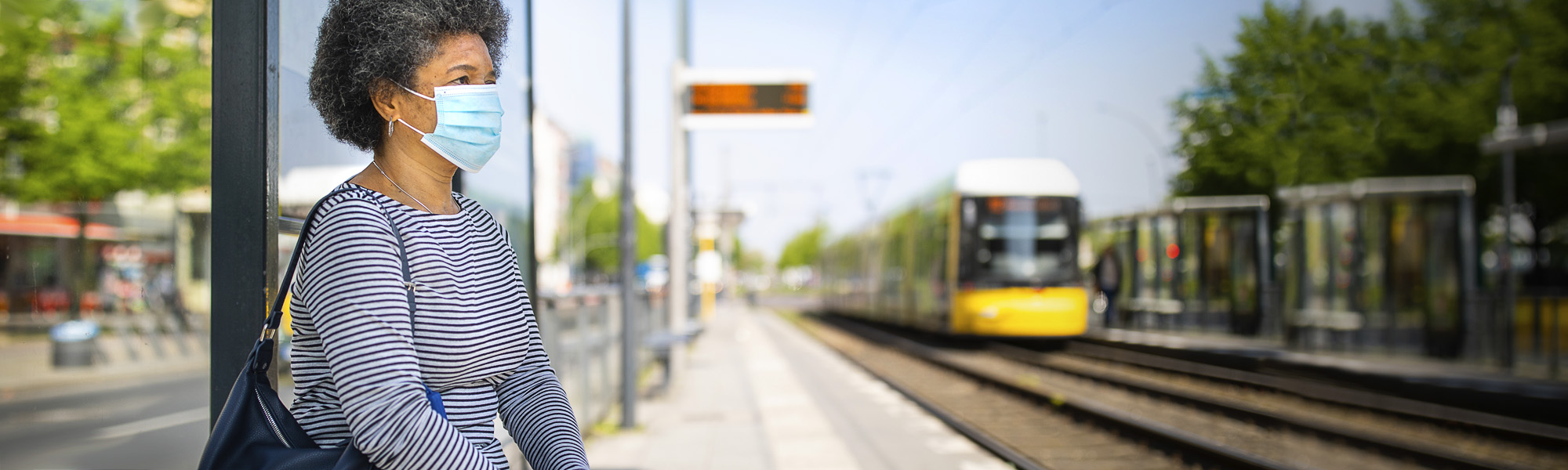 Black woman wearing a mask while standing on a train platform