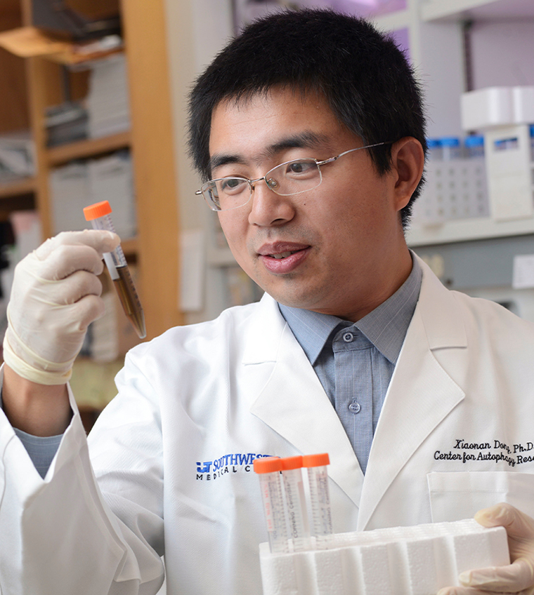 A man with black hair, glasses, wearing lab coat