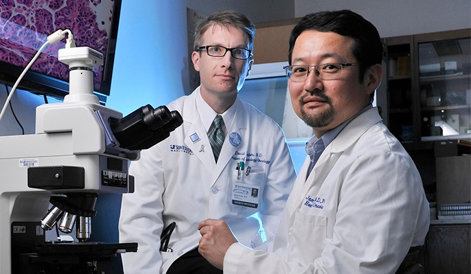 David Gerber, M.D. and James Kim, M.D., Ph.D., who is sitting in front of a microscope