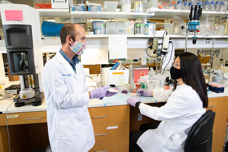 Drs. Ryan Hibbs and Jeong Joo Kim wear masks and white coats in the research lab