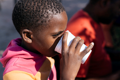 A young child drinks from a white foam cup
