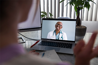 A person looking at a laptop with a Black male doctor on the screen