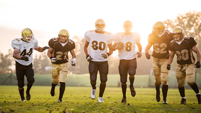 Three football players in white jerseys and black pants and three players in black jerseys and gold pants