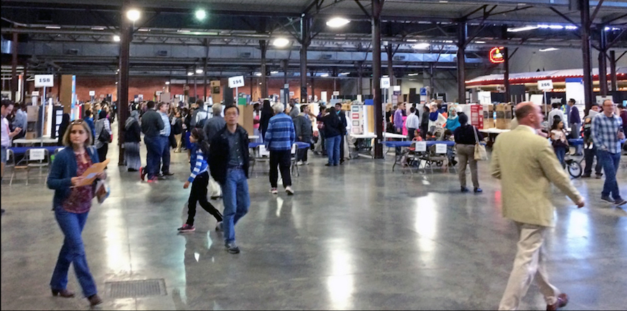 Men and women walk around in a large exhibition area