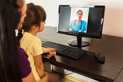 Mother and child sitting at a computer talking with a doctor on the screen