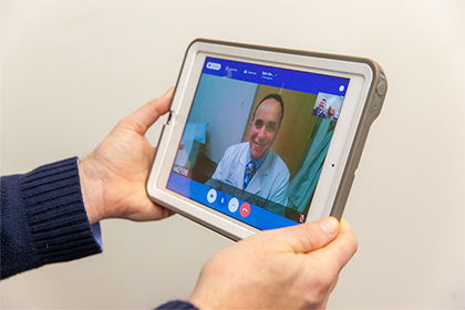 A person holding a tablet with a doctor on the screen