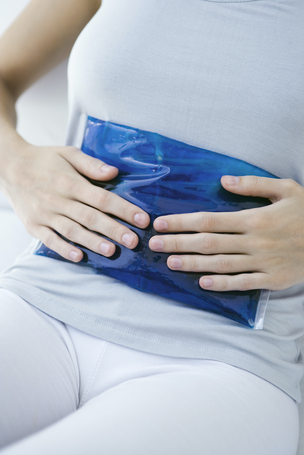 Woman holding ice pack against her stomach, cropped view