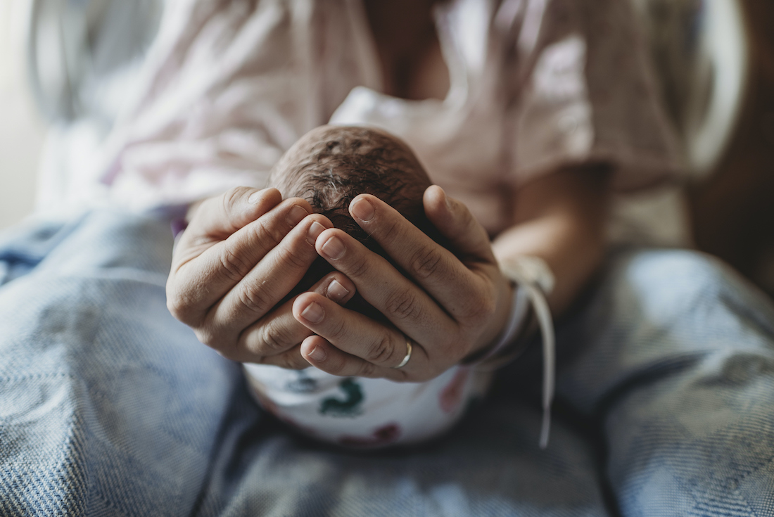 Macro view of mothers hands holding newborn boy's head