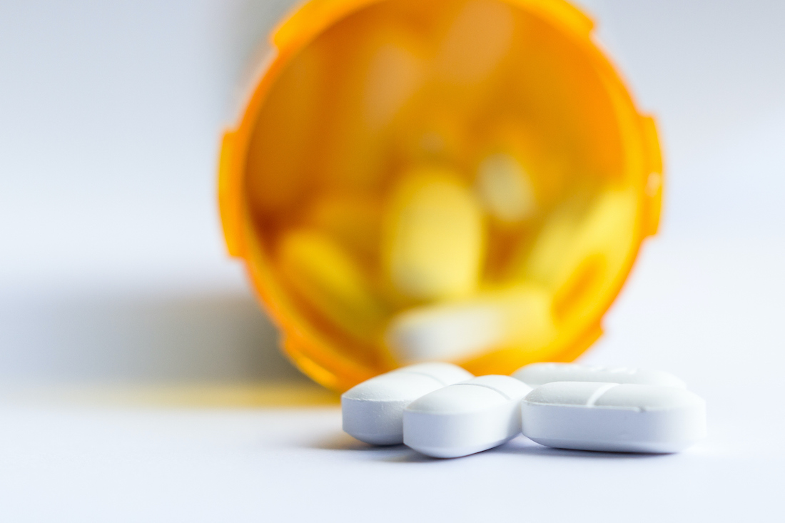 close up of a group of white tablets with an out of focus prescription bottle in the background