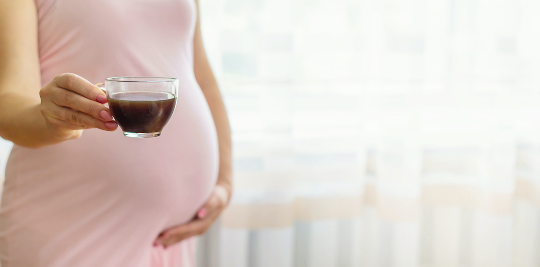 A pregnant woman holding a cup coffee.