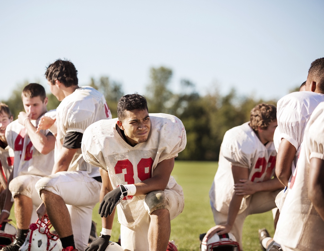Football players kneeling at playing field on sunny day