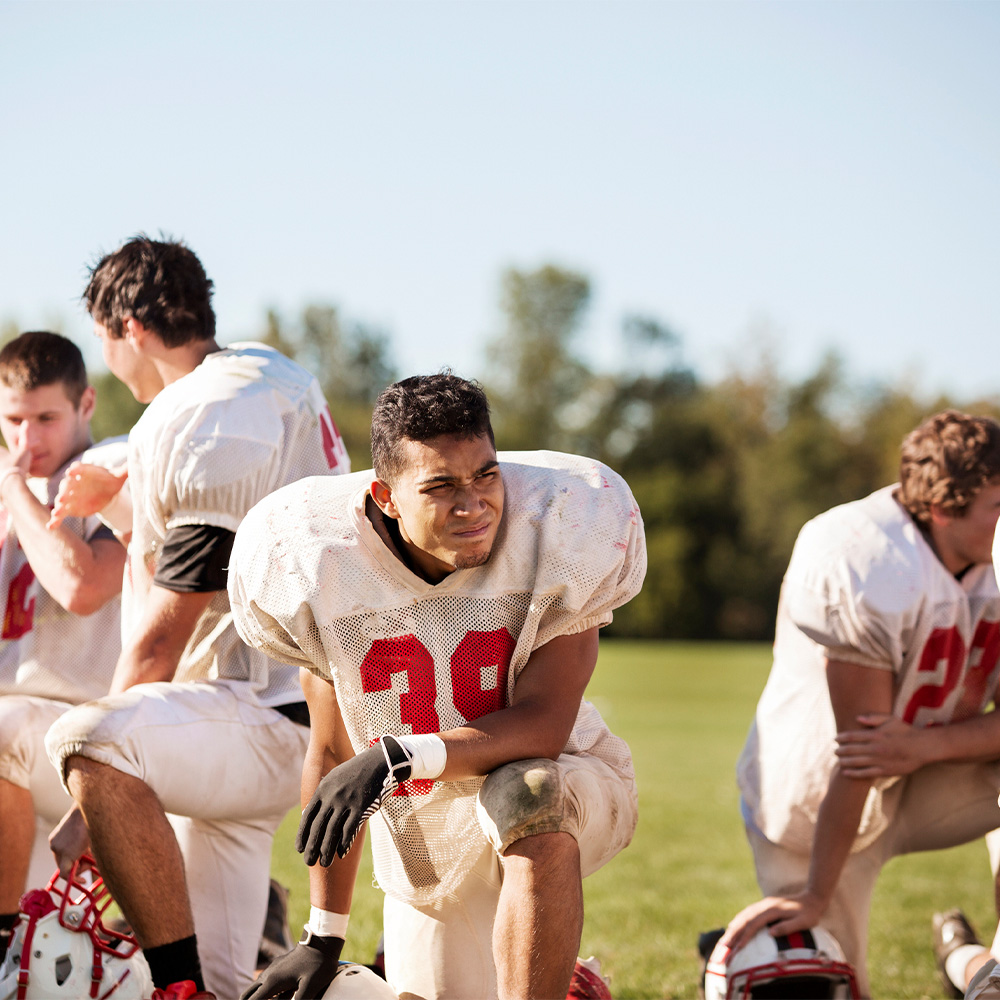 Football players kneeling at playing field on sunny day