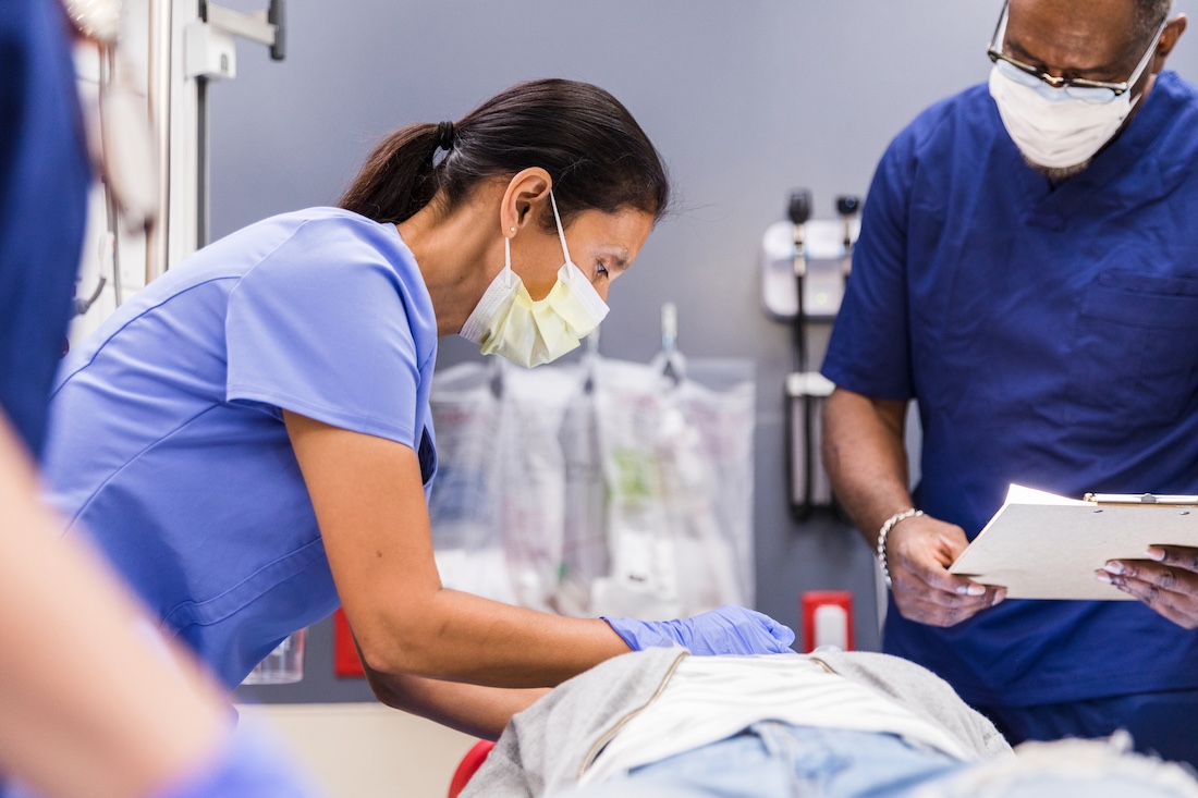 Mature nurse bends over patient as male doctor observes