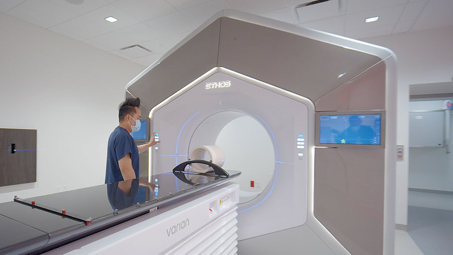 Photo of large hexagonal Ethos Radiation Oncology machine with male technician standing to the left