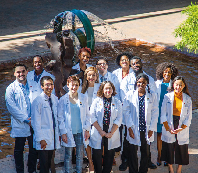 A group of diverse medical professionals in front of a campus water sculpture