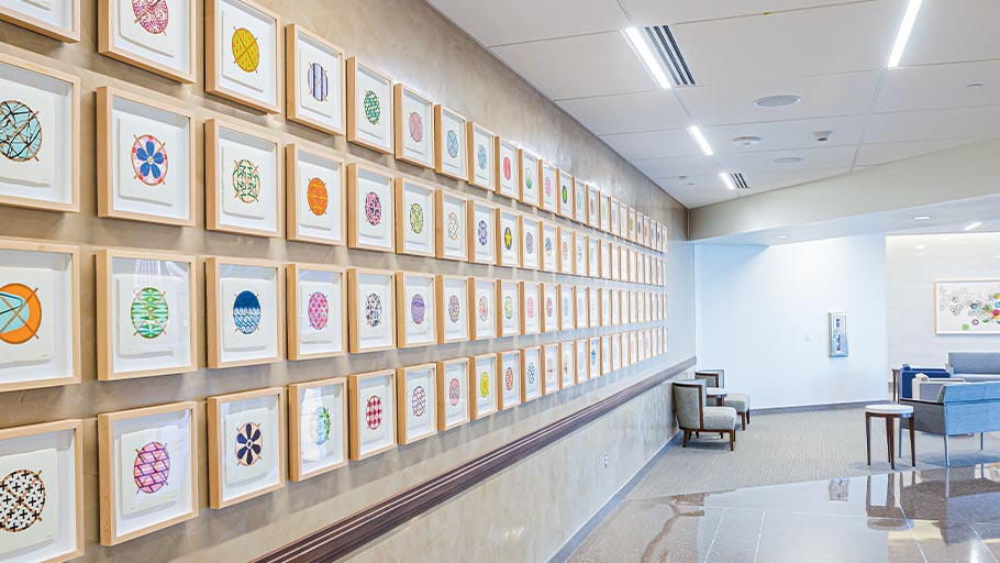 100 equally sized and framed drawings hang on a long wall